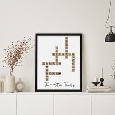 a framed crossword puzzle piece on a wall above a white dresser with vases