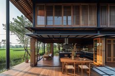 a wooden deck with chairs and table next to an open air kitchen area that overlooks rice fields