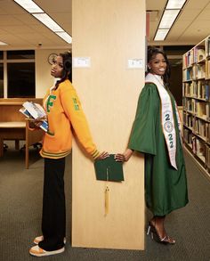 two women dressed in graduation gowns standing next to each other near bookshelves