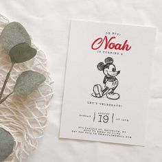 a mickey mouse birthday card on top of a white table cloth with eucalyptus leaves next to it