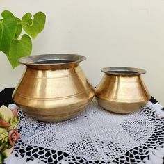 two brass vases sitting on top of a doily next to a potted plant