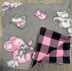 a pink and black checkered blanket with an animal design on the front, sitting on a wooden floor