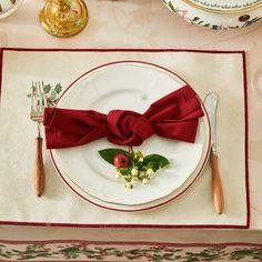 a place setting with red napkins, silverware and flowers on the table cloth