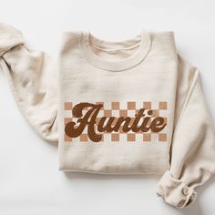 Checkered Auntie Sweatshirt, Retro Auntie Sweater, Gift for Aunt, New Auntie Sweatshirt, Baby Announcement for Aunt, Cool Aunt Sweatshirt  ♥ WHY YOU WILL LOVE YOUR SWEATSHIRT ♥ * Unique cute gift for everyone that is incredibly easy and stress-free to order & receive * Design is a the words Golden mama writing with trendy retro color and font. * Softest quality 50% cotton, 50% polyester with loose fit that runs true to size (unisex) * Extreme comfort with no bulky side seams for great shape and Retro Fall Tops With Lettering, Retro Lettering Tops For Fall, Fall Crew Neck T-shirt With Name Print, Retro Crew Neck Tops With Name Print, Long Sleeve Tops With Name Print For Fall, Retro Cotton Tops With Name Print, Long Sleeve Name Print Tops For Fall, Winter Cotton Top With Name Print, Cotton Top With Name Print For Winter