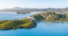 an island in the middle of water surrounded by trees and buildings with mountains in the background