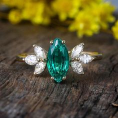 an emerald and diamond ring sitting on top of a wooden table next to yellow flowers