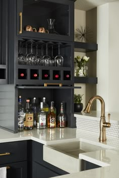 a kitchen with black cabinets and gold faucet, wine glasses on the shelf