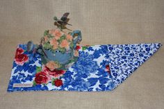 a blue and white flowered pot holder on top of a placemat with a bird perched on it