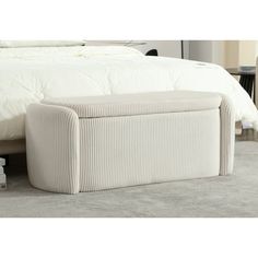 an upholstered bed with a white blanket and pillows on the floor next to it