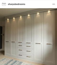 a large white closet with many drawers and lights on the wall above it, in an empty room