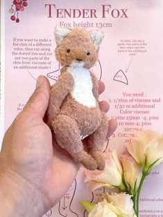 a hand holding a small teddy bear next to a white and yellow flower with information on it