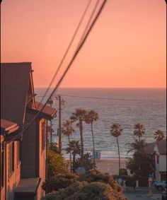 the sun is setting over the ocean with houses and palm trees in front of it