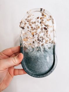 a hand holding a clear case with seashells in it and sand on the bottom