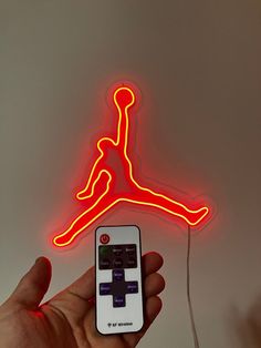 a hand holding a remote control in front of a neon air jordan logo on the wall