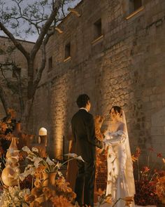 a bride and groom standing in front of an old brick building with flowers on the ground