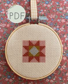 the cross stitch pattern is being displayed in front of a flowery background with a white ribbon