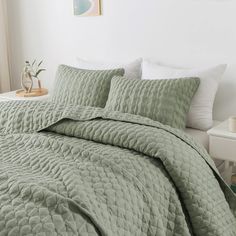 a bed with green bedspread and pillows in a white room next to a window