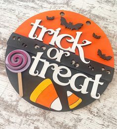 a trick or treat sign with candy and bats around it on a wooden table top