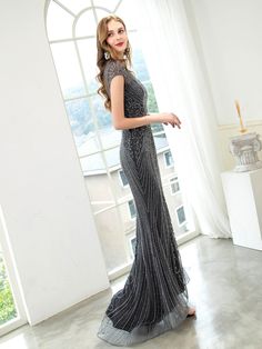 a woman standing in front of a window wearing a long dress with sequins