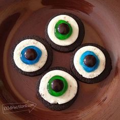 four decorated cookies with googly eyes and chocolate on top in a brown bowl, ready to be eaten