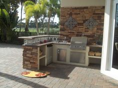 an outdoor kitchen with grill, sink and table in the middle of a brick patio