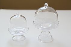 two clear glass dishes sitting on top of a white table next to an empty one