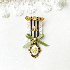 a white and black striped ribbon with a gold brooch hanging from it's center