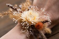 a person's hand holding a flower with white and brown flowers on the wrist