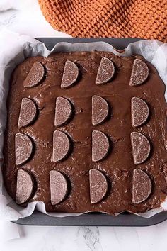 a chocolate cake in a pan on top of a white table with an orange towel next to it