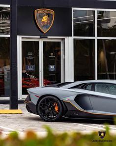 a grey sports car parked in front of a building with the lamb logo on it