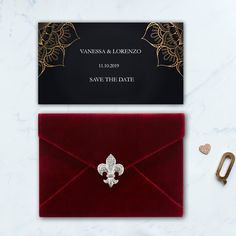 a red envelope with a gold fleur de lis brooch on it and a black save the date card