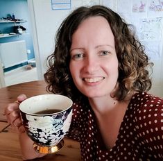 a woman sitting at a table with a cup of coffee in her hand and smiling