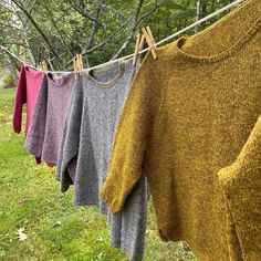 several sweaters hanging on a clothes line in front of green grass and trees,