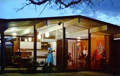 two people standing in the doorway of a modern house at night with an open kitchen and dining area