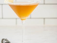 an orange drink in a martini glass next to a pair of tennis shoes on the floor