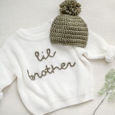 a knitted sweater and hat with the word be winter written on it next to a plant