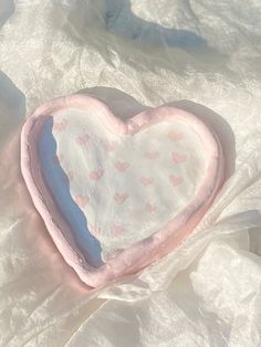 a pink heart shaped pillow sitting on top of a white cloth covered bedding sheet