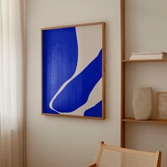 a blue and white painting hangs on the wall next to a chair in front of a window