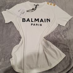 Nwt ,100% Authentic Balmain Shirt, Size Xl. The Parisian Brand Glams Up A Staple Cotton Tee With A Foiled Logo And A Trio Of Crested Buttons At One Shoulder. Crewneck Short Sleeves 100% Cotton Machine Wash, No Returns. Elegant White Shirt With Graphic Print, Designer White T-shirt For Spring, Luxury White Tops For Summer, Luxury White Summer Tops, Luxury White Summer Shirt, Balmain Shirt Outfit Women, Balmain Top Outfit, Balmain Accessories, Balmain Shirt