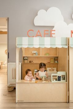 two children playing in a play kitchen with the word cafe on it's wall