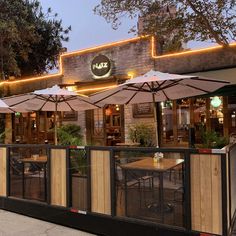 the outside of a restaurant with umbrellas and tables in front of it at dusk