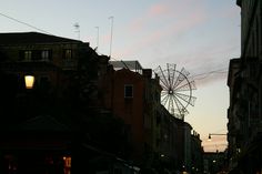 a street scene with buildings and a ferris wheel in the distance at dusk or dawn