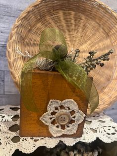 a wooden box with a green ribbon and some flowers in it sitting on a doily