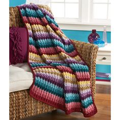 a crocheted blanket sitting on top of a wicker chair next to a window