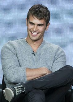 a man sitting in a chair with his arms crossed and looking at the camera while smiling