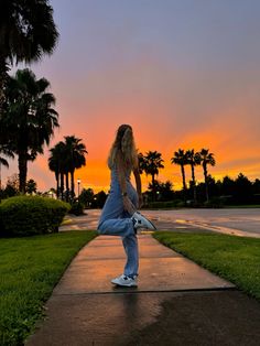 a woman standing on the sidewalk in front of palm trees at sunset with her legs spread out