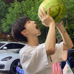 a young man holding up a watermelon in front of his face and mouth