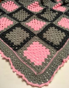 a crocheted blanket with pink and gray designs on it sitting on a table