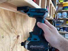 a man is holding a drill in front of a wooden shelf with tools on it