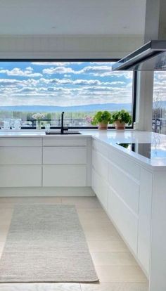 a kitchen with white cabinets and an area rug in front of the window that looks out onto water